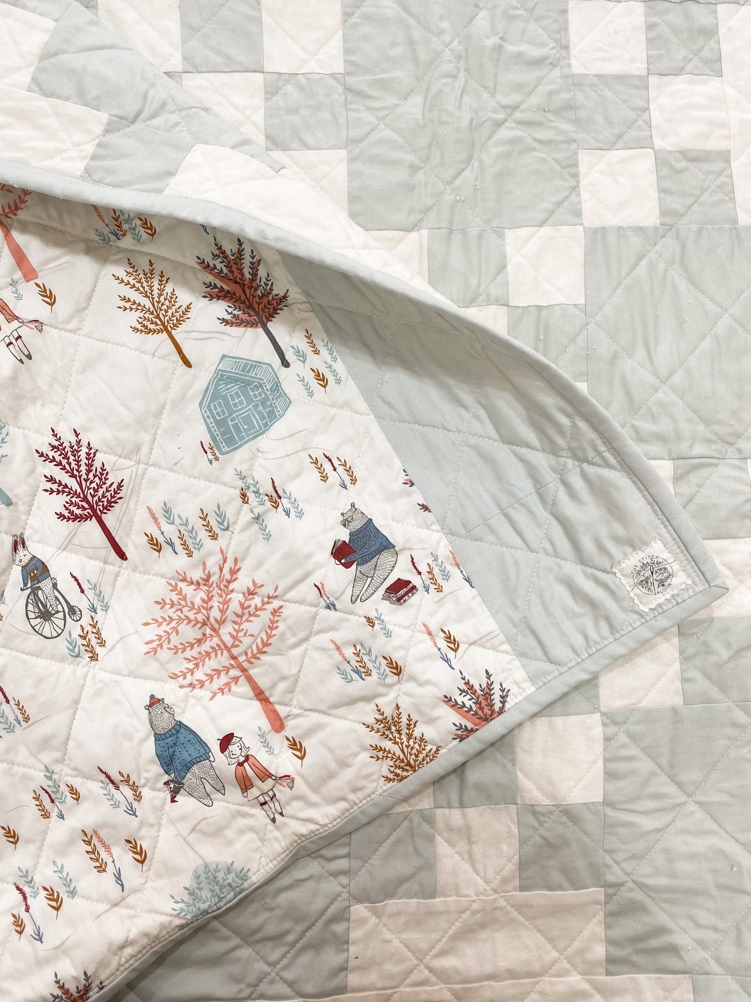 Close up of quilt with light green sage and white squares with woodland print backing